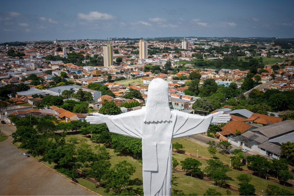 Estátua branca do Cristo de braços abertos vista de cima, com a cidade de Avaré e seus prédios ao fundo
