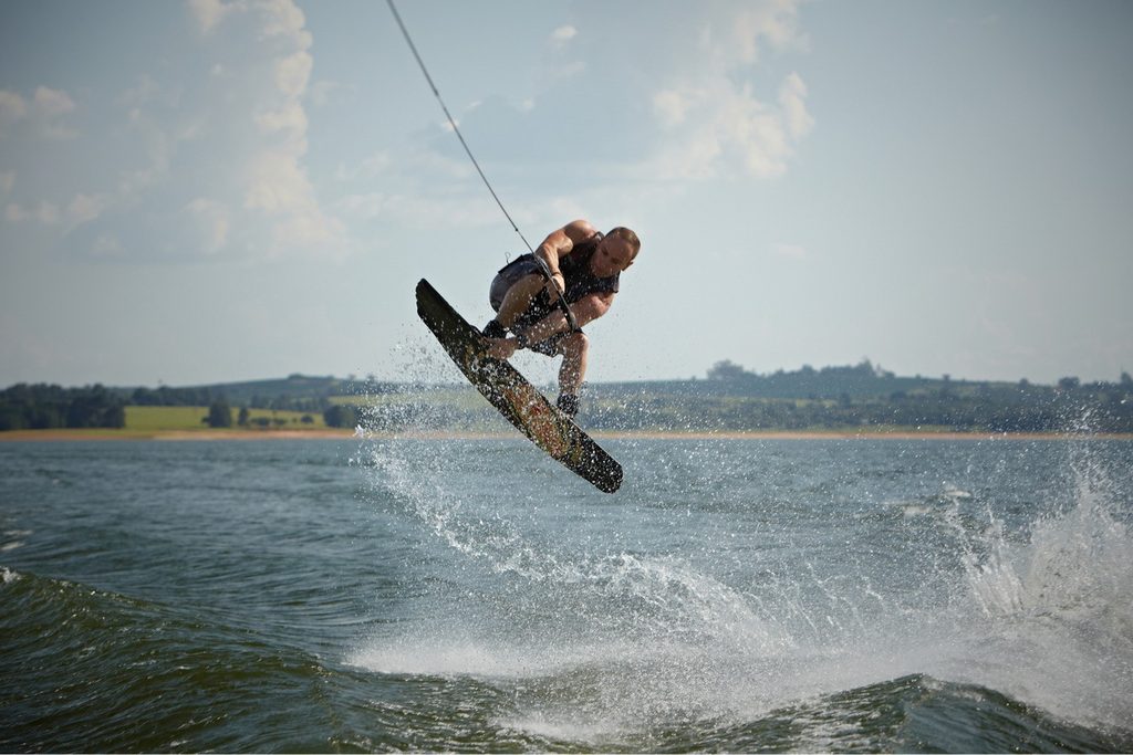 Homem saltando com prancha de wakeboard sobre a água da Represa de Jurumirim, em Avaré