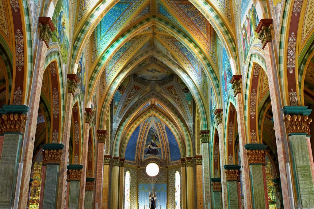 Interior do Santuário Nossa Senhora das Dores, com arcos góticos pintados em cores vivas e vitral redondo no altar