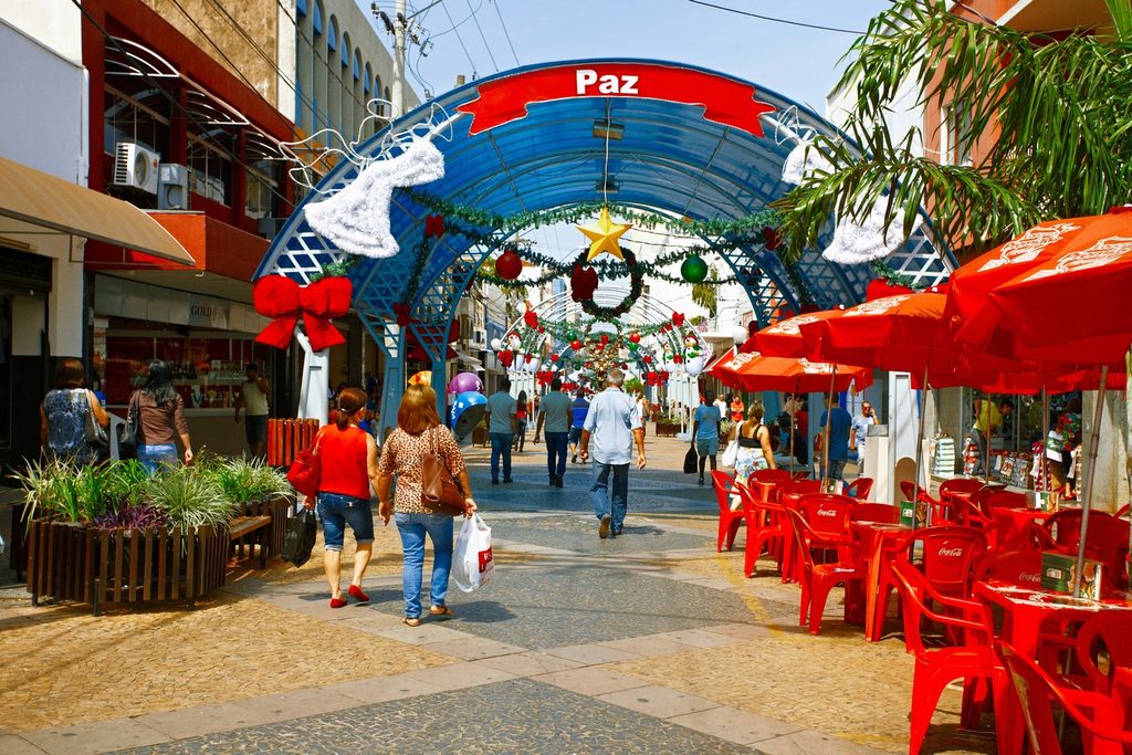 Rua de pedestres com lojas, mesas vermelhas e arco azul decorado para o Natal, no Calçadão da Batista de Carvalho