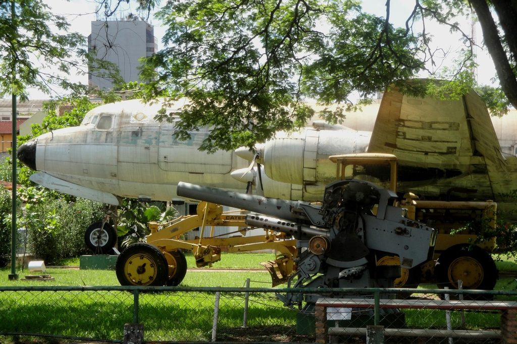 Avião quadrimotor prateado da VASP no pátio do museu, com um canhão e uma motoniveladora amarela em frente