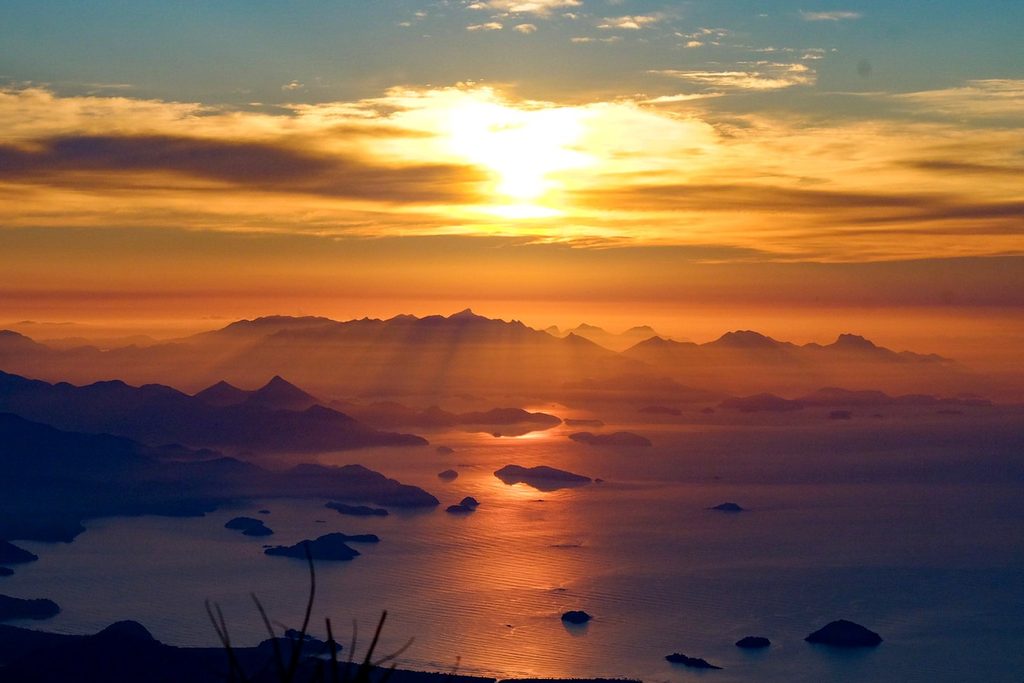 Sol baixo sobre o mar com ilhas e montanhas em camadas, visto do alto da Serra da Bocaina