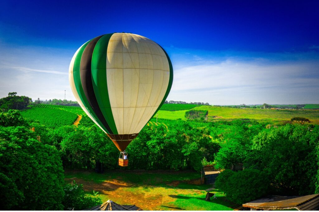 Balão de ar quente verde e branco descendo sobre campos e plantações verdes em Boituva