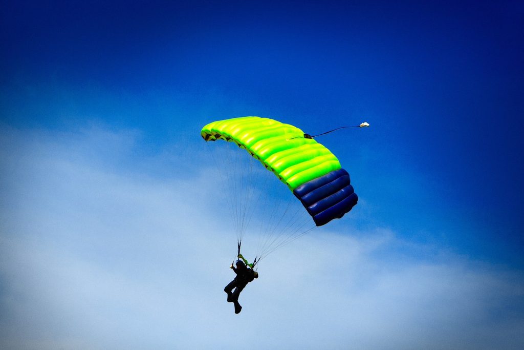 Paraquedista com velame verde e azul descendo no céu azul de Boituva