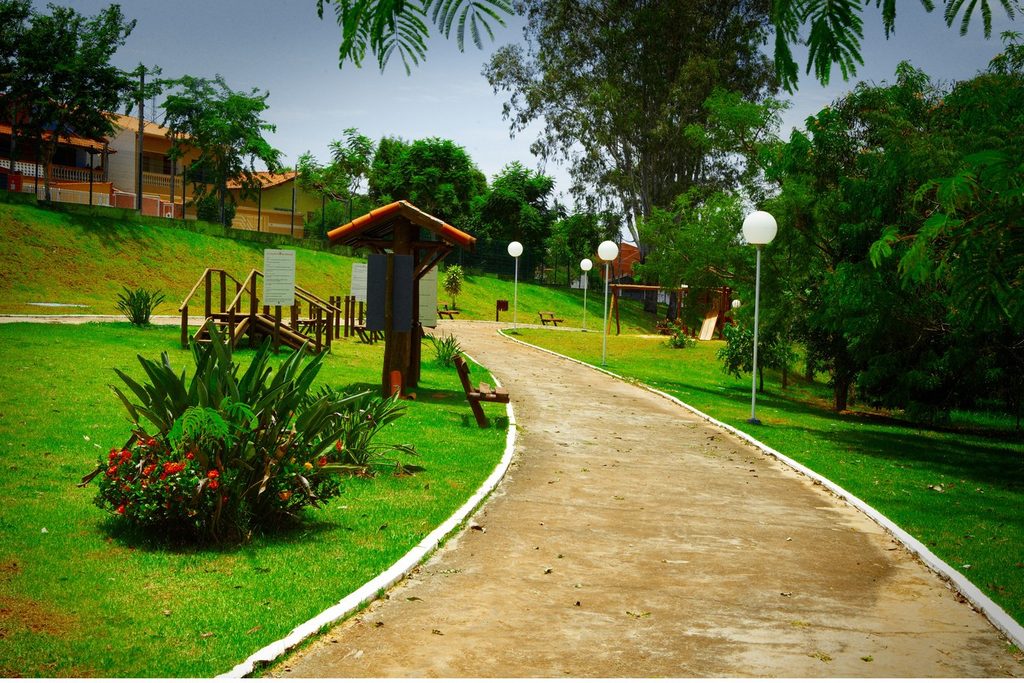 Caminho de cimento entre gramado, jardins e postes de luz no Parque da Cidade Egídio Labronici