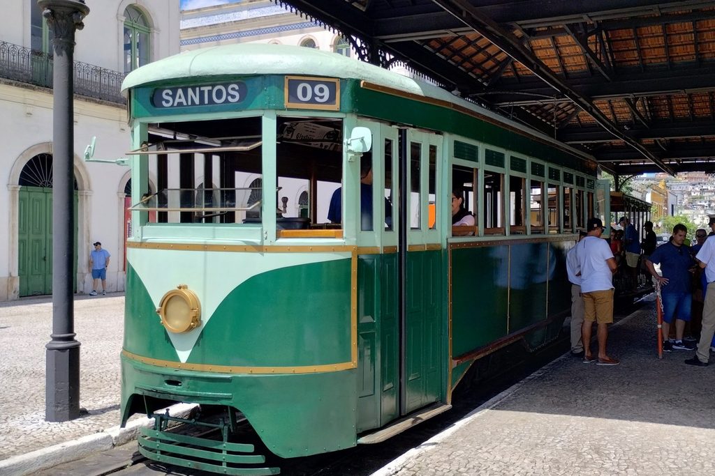 Bonde antigo verde e branco número 09, com a placa Santos, parado na plataforma coberta da Estação do Valongo com passageiros embarcando