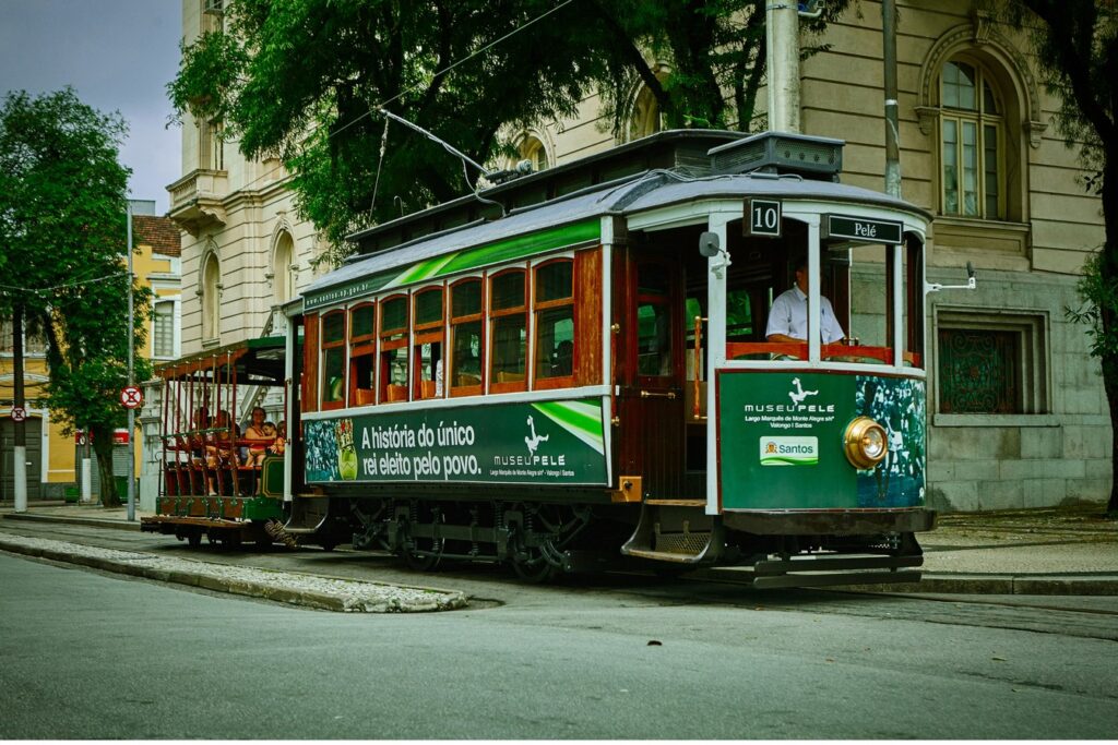 Bonde de madeira verde e vermelho da linha turística circulando por uma rua do centro histórico de Santos, ao lado de prédios antigos
