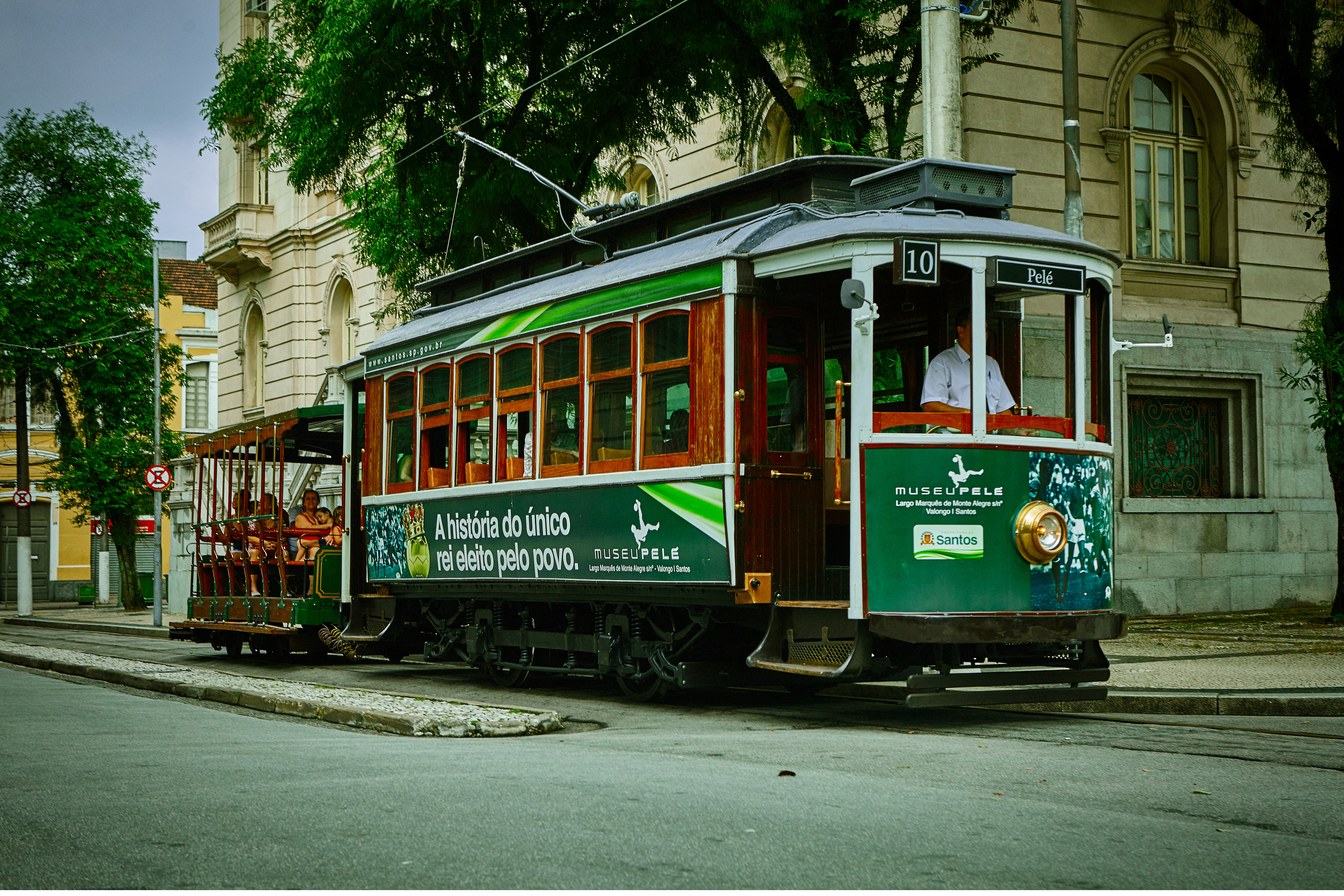 Bonde de madeira verde e vermelho da linha turística circulando por uma rua do centro histórico de Santos, ao lado de prédios antigos