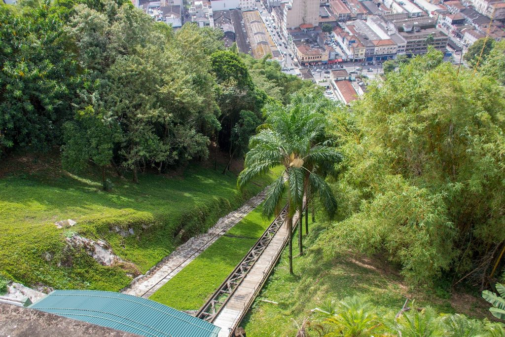 Trilhos do funicular descendo o morro entre palmeiras e mata, com o centro de Santos lá embaixo