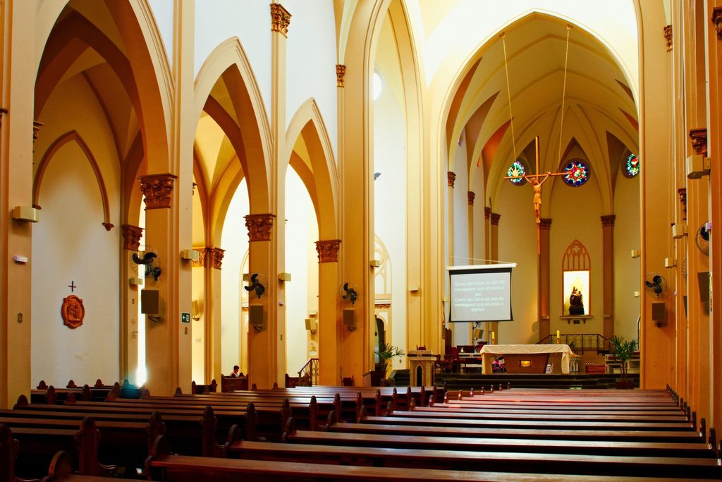 Nave da Basílica de Sant'Ana, em Botucatu, com arcos góticos claros, bancos de madeira e vitrais no altar