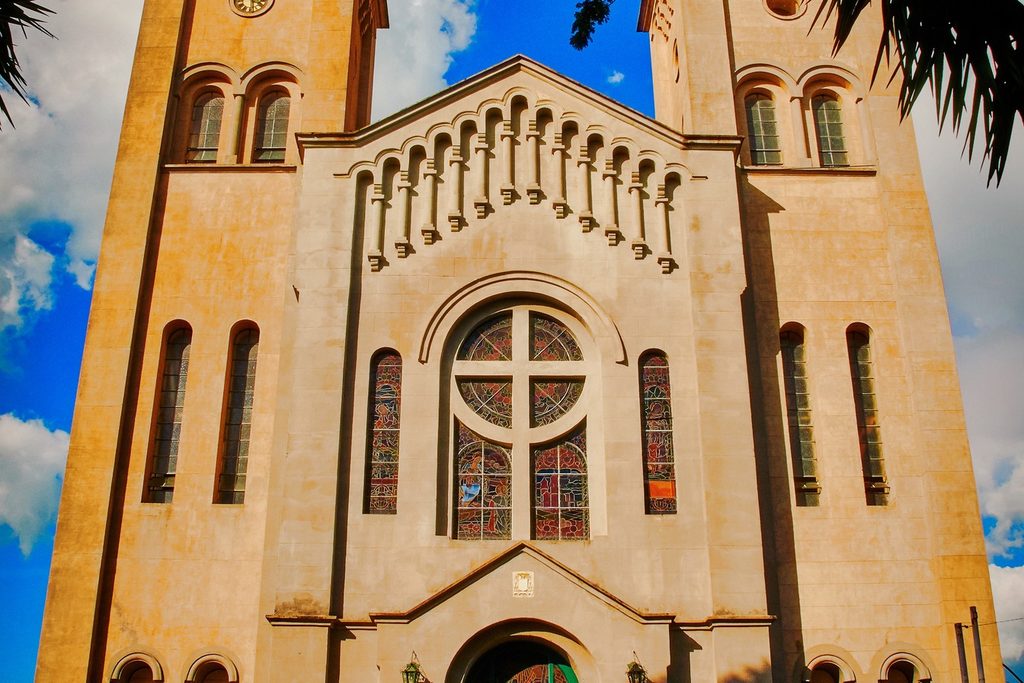 Fachada clara de igreja com duas torres, rosácea com vitral e arcos, no Largo do Rosário