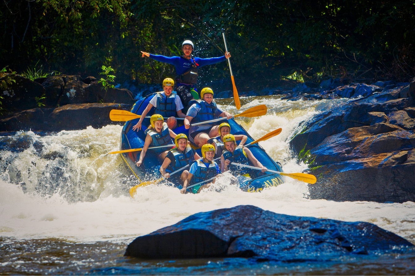 Bote de rafting com seis pessoas de capacete e colete descendo uma corredeira de água branca no rio Jacaré-Pepira, em Brotas