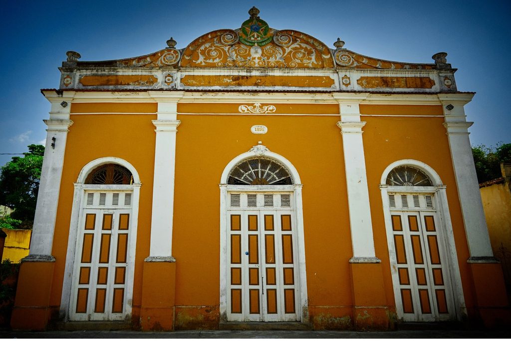 Fachada laranja e branca do Teatro Municipal de Cachoeira Paulista, de 1883, com portas em arco