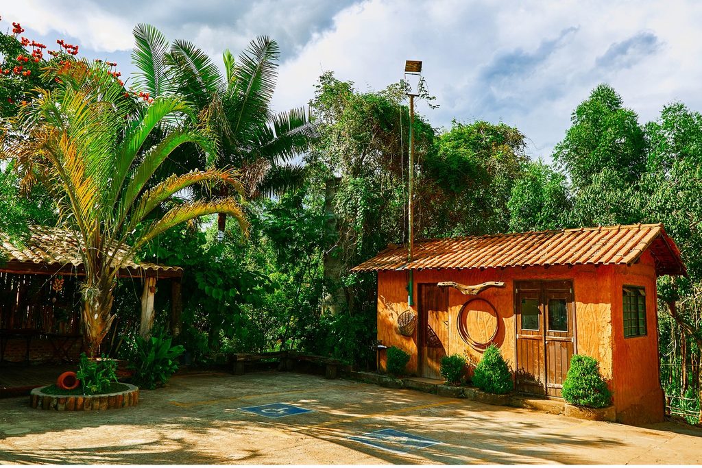 Casinha de tijolo laranja com porta de madeira e jardim de palmeiras na Pizza na Roça, em Caconde