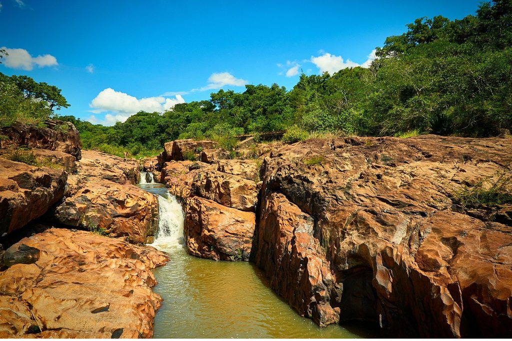 Pequena queda d'água entre grandes rochas alaranjadas formando poços naturais na Usina Velha de Caconde