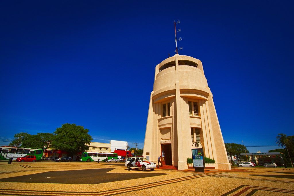 Torre do Castelo, antigo reservatório de água bege com mirante no alto, numa praça com piso de pedras portuguesas sob céu azul