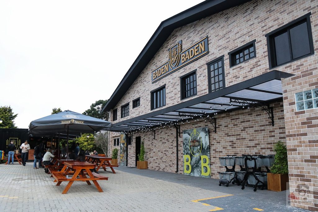 Fachada de tijolos da cervejaria Baden Baden com mesas de madeira e guarda-sol na calçada