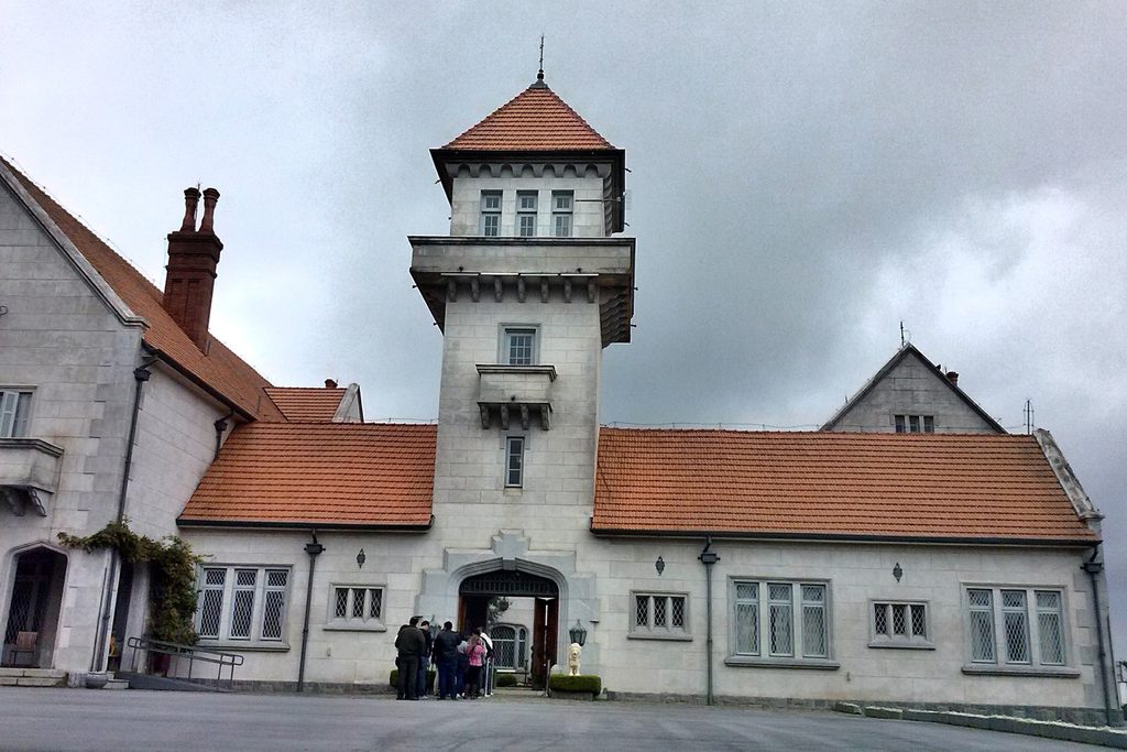 Palácio Boa Vista, em Campos do Jordão, com paredes claras, telhado de telhas vermelhas e torre central, e visitantes na entrada em dia nublado