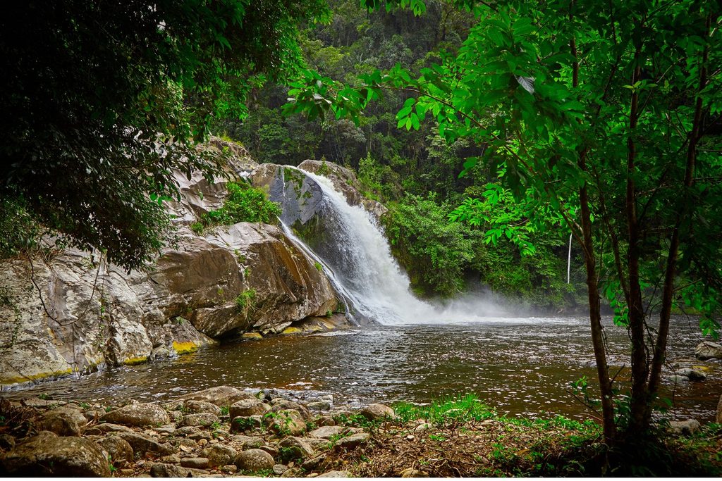Cachoeira do Rio das Minas caindo entre pedras num poço cercado de mata atlântica