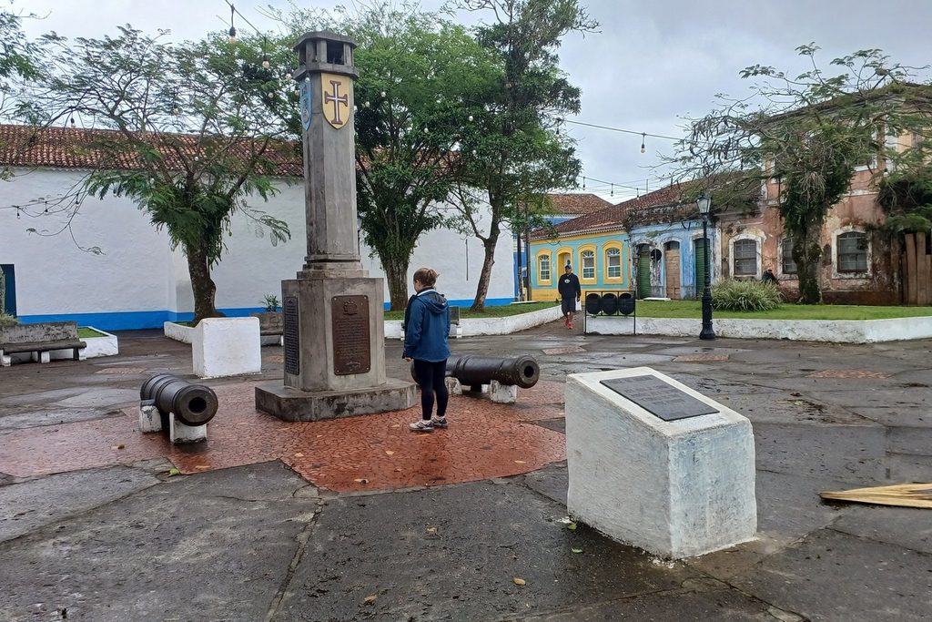 Largo com um marco de pedra e dois canhões antigos, com casarões coloniais ao fundo