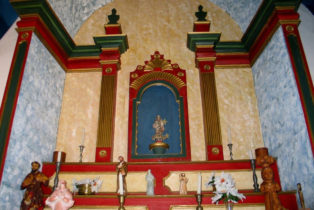 Altar colorido em tons de vermelho, verde e dourado, com nicho e imagens de santos, na Fazenda Capoava