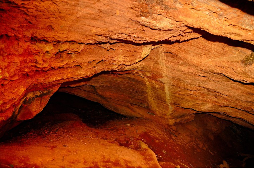 Abertura baixa de uma pequena caverna de rocha alaranjada, a Toca da Onça