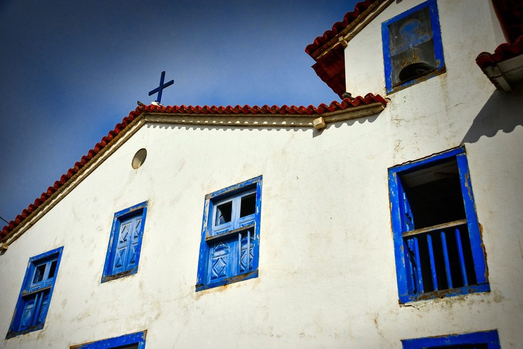 Fachada branca da Igreja de Nossa Senhora do Rosário, com janelas azuis, telhado de telhas e cruz no alto