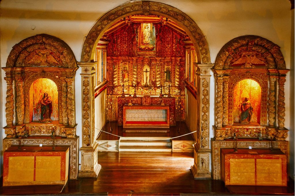 Altar-mor e altares laterais de talha dourada e pintada, com imagens de santos, no interior da igreja jesuíta de Embu das Artes