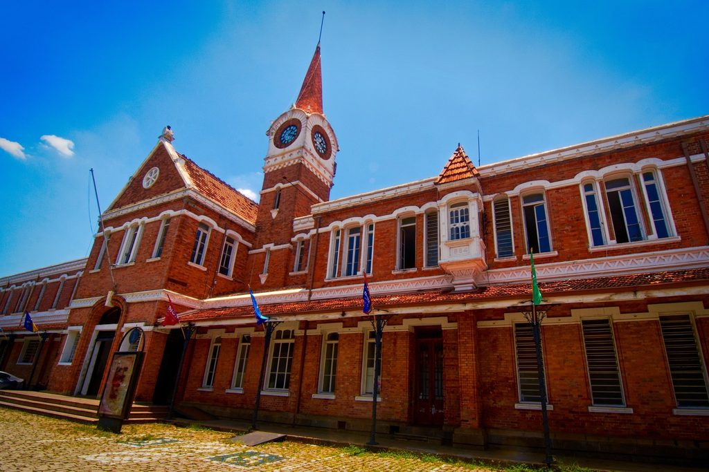 Prédio de tijolos vermelhos da Estação Cultura, em Campinas, com torre de relógio pontiaguda e bandeiras na fachada