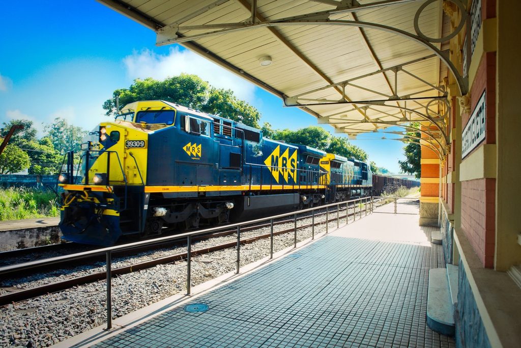 Locomotiva de carga azul e amarela passando ao lado da plataforma coberta da estação de Guaratinguetá