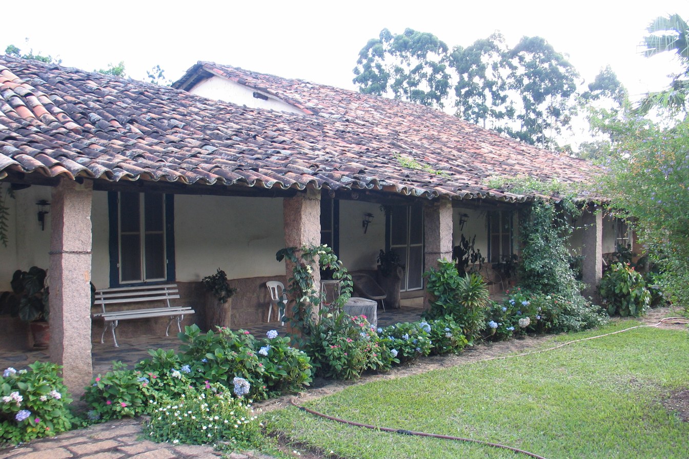 Varanda comprida da sede da Fazenda Concórdia, com telhado colonial, colunas e canteiros de flores na frente