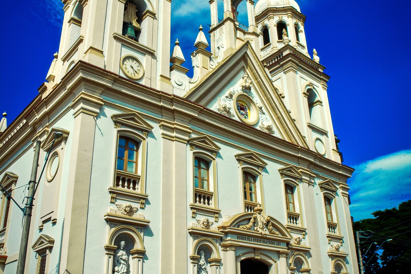 Fachada clara e ornamentada da Catedral de Santo Antônio, em Guaratinguetá, com torres, relógio e estátuas, sob céu azul