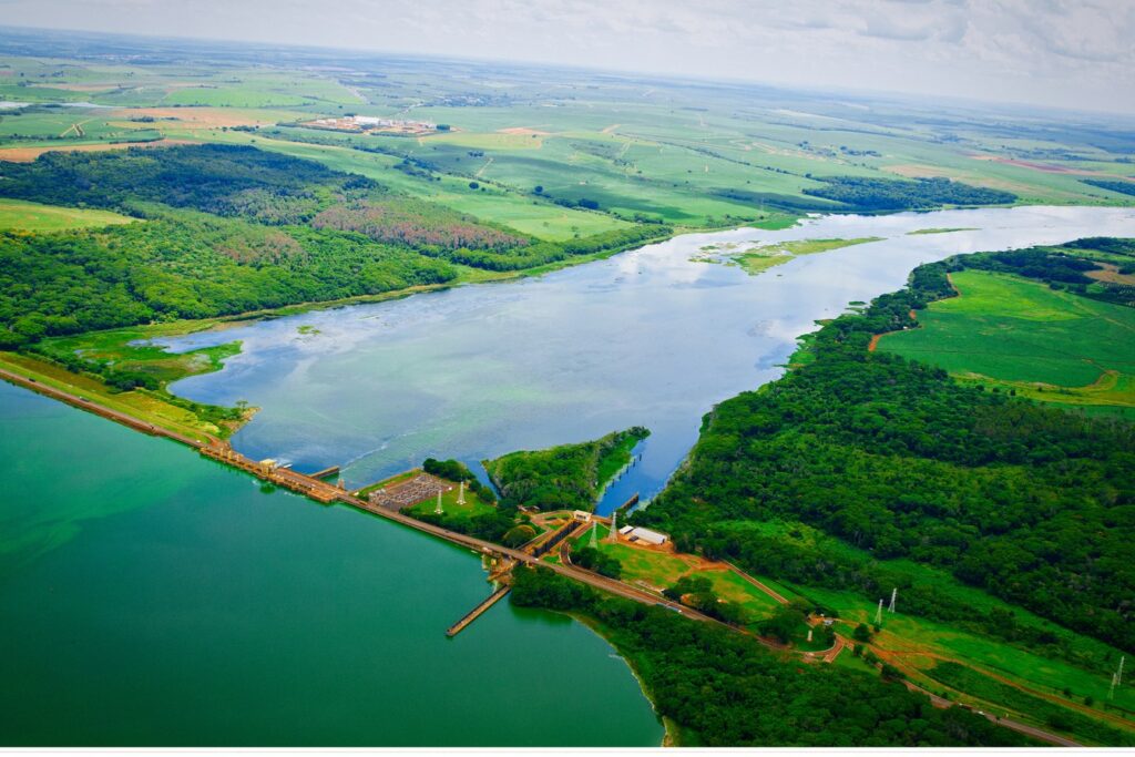 Vista aérea da barragem da usina hidrelétrica de Ibitinga no Rio Tietê, com a represa verde de um lado e o rio entre matas do outro