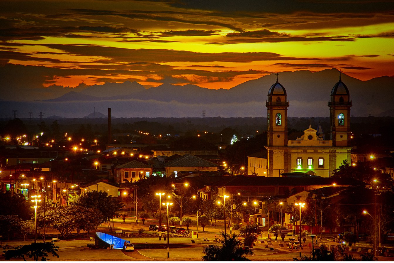 Centro histórico de Iguape iluminado ao entardecer, com as duas torres da Basílica do Bom Jesus e a serra sob um céu alaranjado