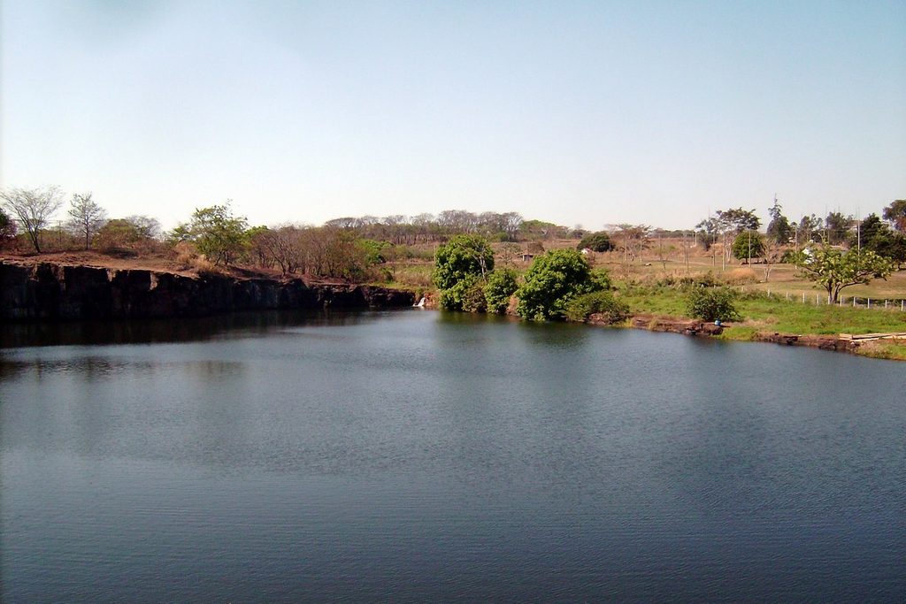 Lago de águas calmas com paredão de pedra baixo e vegetação na margem