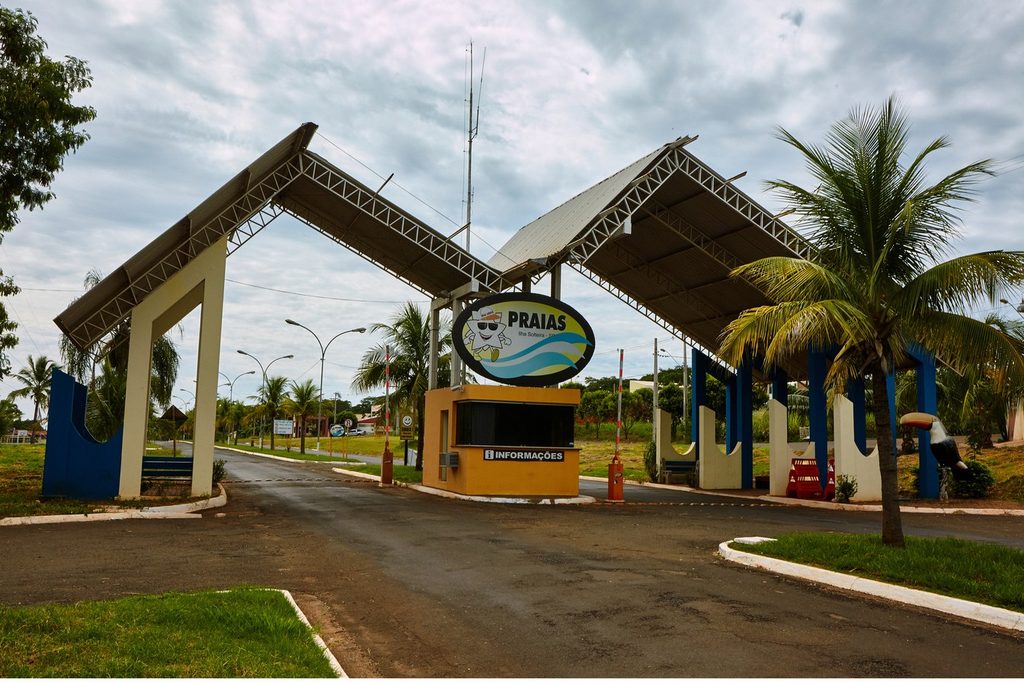 Portal de entrada das praias de Ilha Solteira, com placa colorida, palmeiras e guarita de informações
