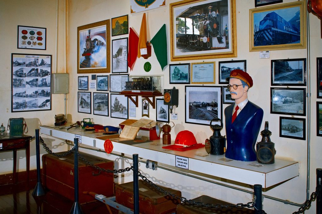 Sala do Museu Ferroviário de Indaiatuba com fotos antigas de trens nas paredes, lampiões, quepes e um boneco de ferroviário