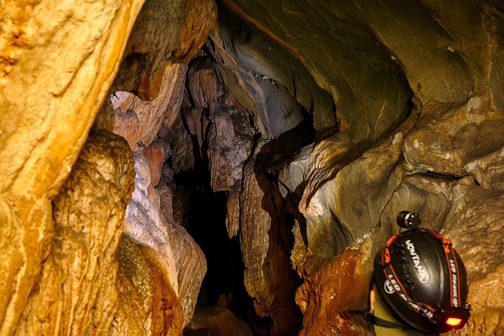 Interior de gruta com rochas em tons de laranja e cinza e um capacete com lanterna em primeiro plano, numa caverna de Intervales
