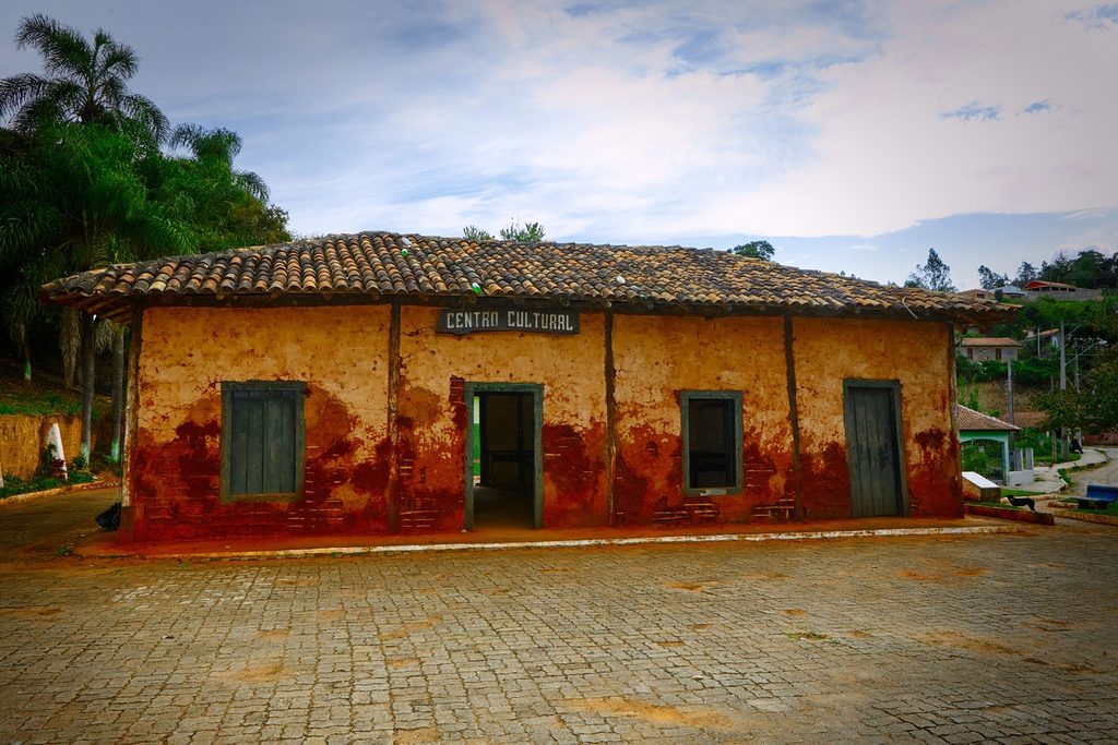 Casa térrea de pau a pique com paredes de barro avermelhado, janelas verdes e telhado de telhas, com a placa Centro Cultural, em Ribeirão Grande