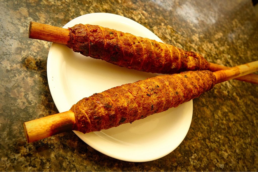 Dois espetos de rojão, carne de porco assada enrolada em espeto de madeira, num prato branco, prato típico da região de Intervales