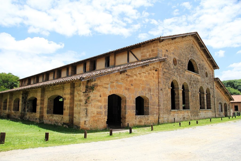 Grande prédio comprido de pedra com janelas e portas em arco e telhado de telhas, no conjunto histórico da Real Fábrica de Ferro