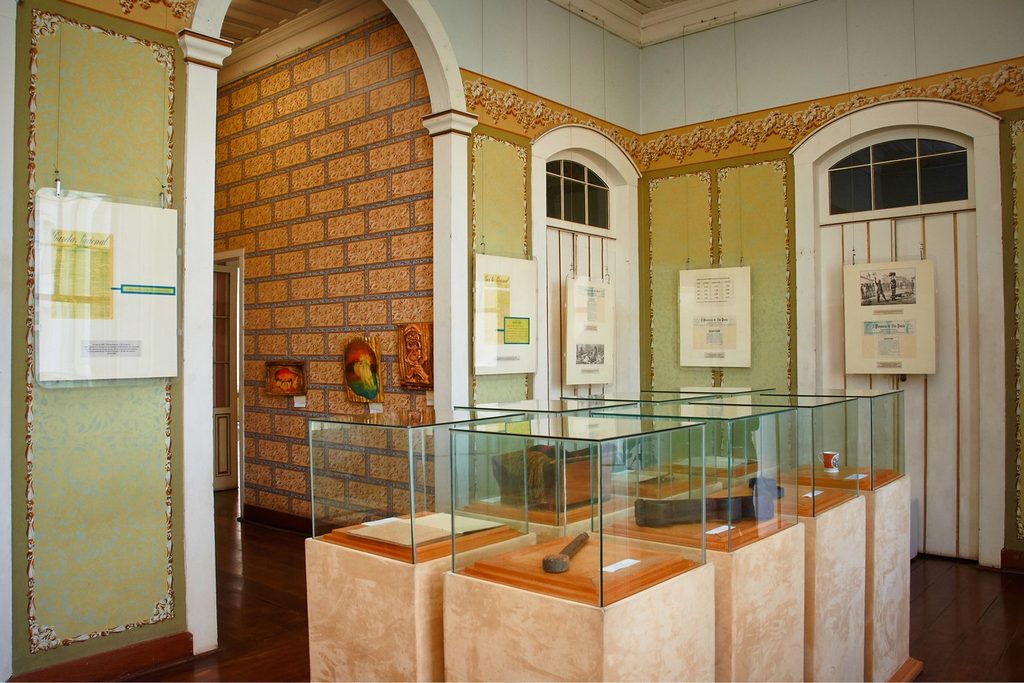 Sala do Museu Histórico Padre Francisco de Paula Lima com vitrines de vidro, quadros antigos e paredes decoradas