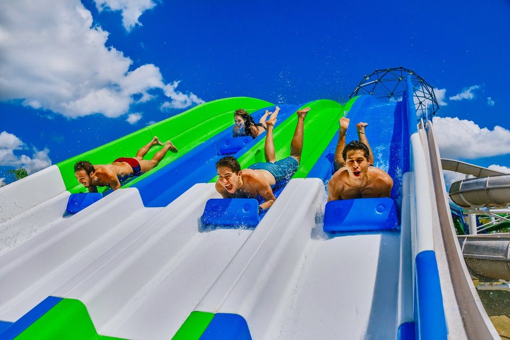 Pessoas descendo de bruços num toboágua largo de raias azuis e verdes no Wet'n Wild, em Itupeva