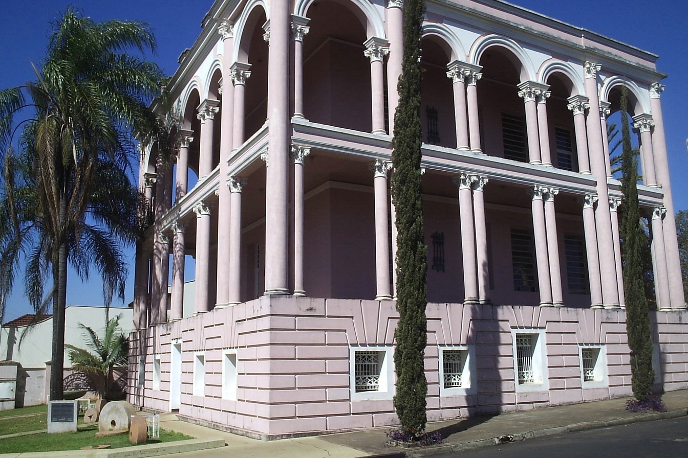 Palacete cor-de-rosa de vários andares com colunas e arcadas, cercado de palmeiras, em Jaboticabal
