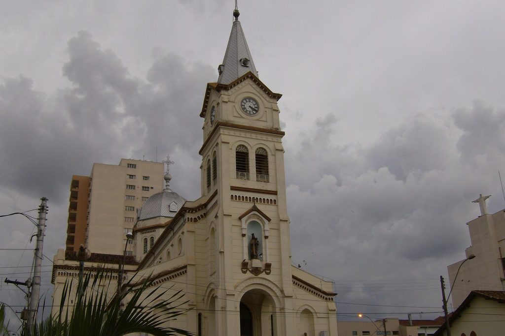 Fachada clara da Catedral Nossa Senhora do Carmo, com torre de relógio e pináculo, sob céu nublado