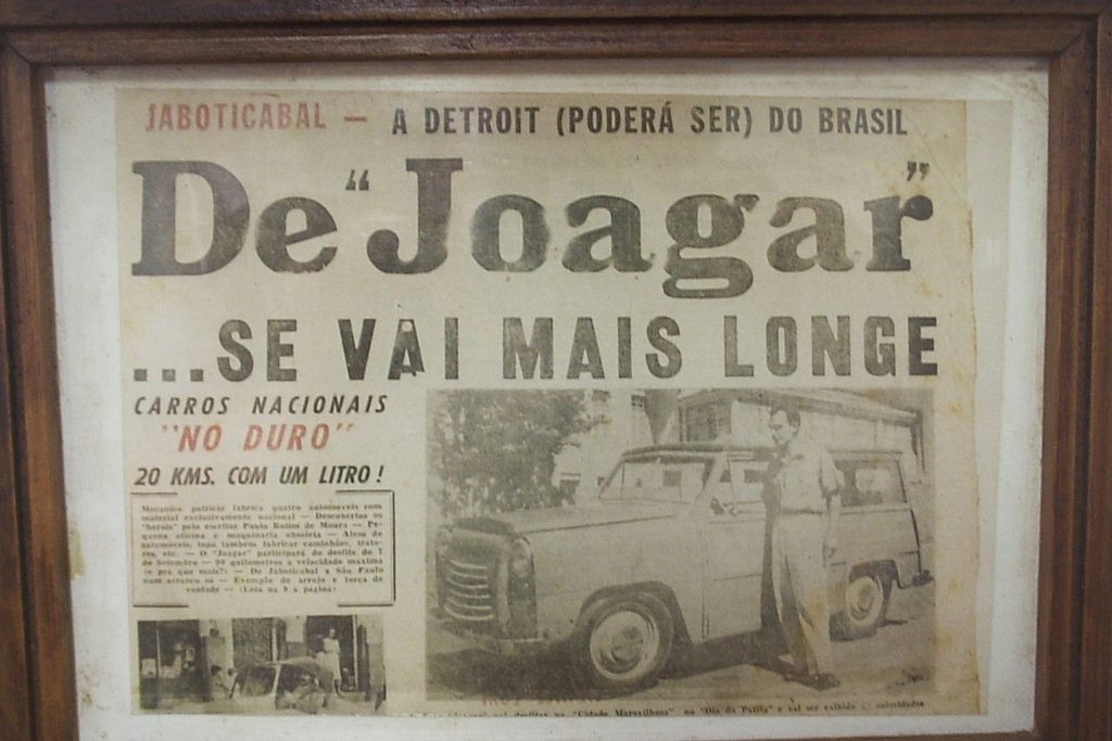 Recorte de jornal antigo emoldurado com a manchete De Joagar se vai mais longe e a foto de uma caminhonete