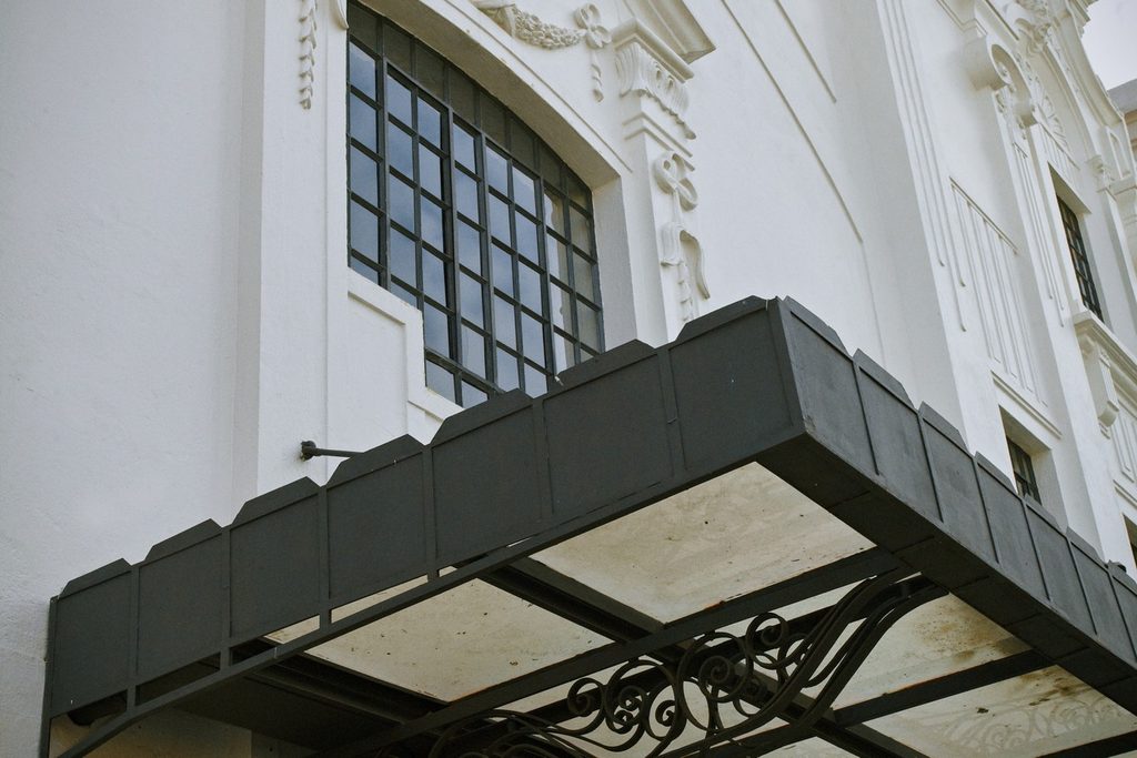Detalhe da fachada branca do Teatro Polytheama, com janela de vidro em arco e marquise de ferro trabalhado