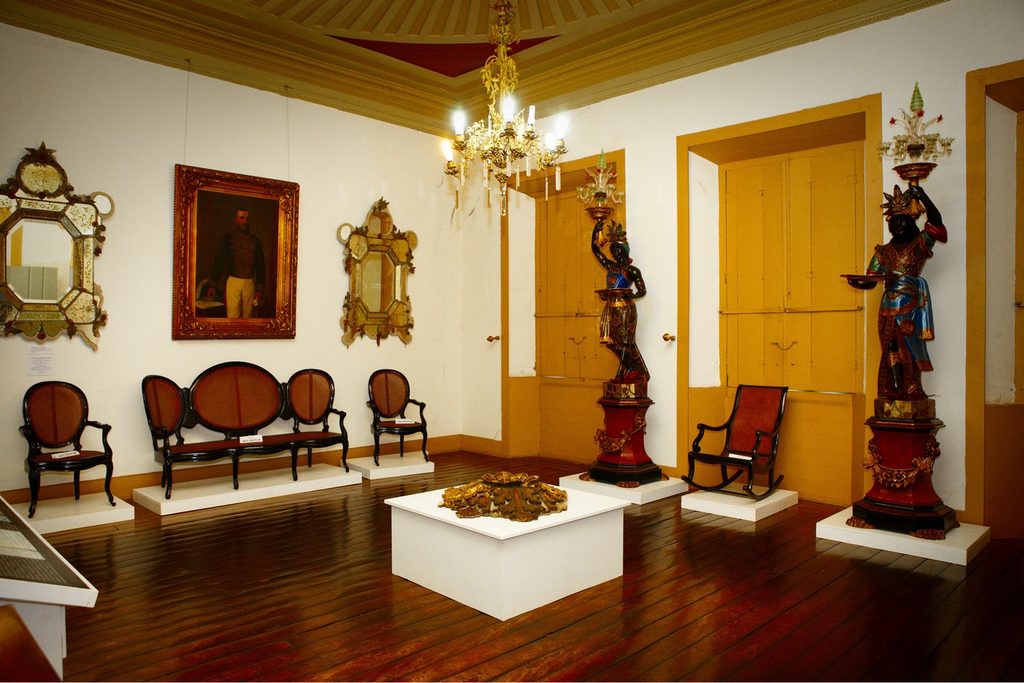 Sala do Solar do Barão, em Jundiaí, com sofá e cadeiras antigas, retrato a óleo, espelhos dourados e lustre de cristal