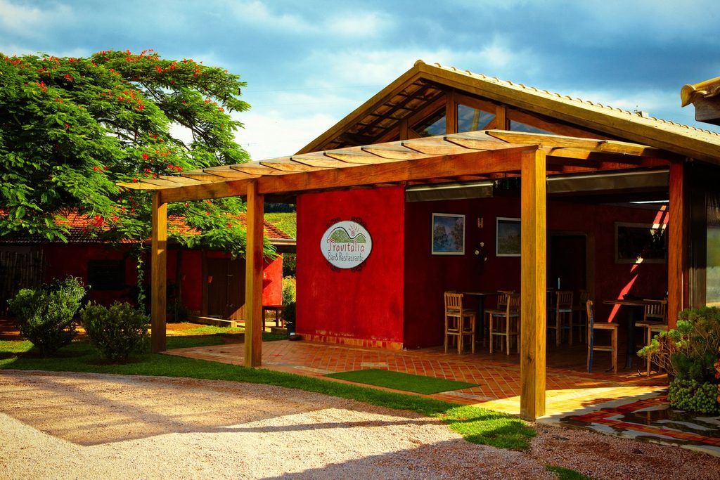 Restaurante Travitália, em Jundiaí, com parede vermelha, pergolado de madeira e jardim com árvore florida