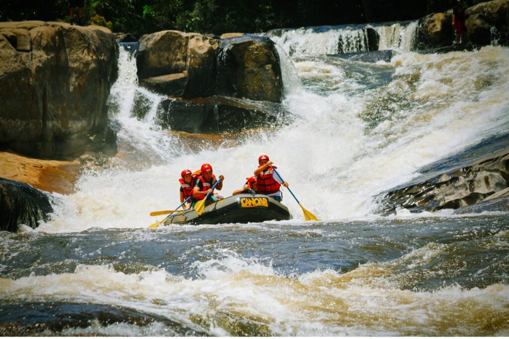 Bote de rafting com quatro pessoas de capacete vermelho descendo uma corredeira entre pedras em Juquitiba